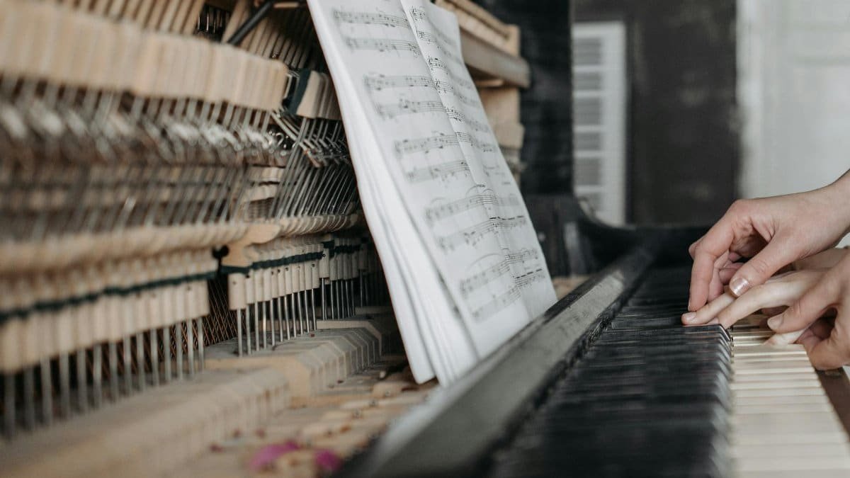 Close-up of hands playing piano keys with open sheet music, emphasizing learning and teaching.