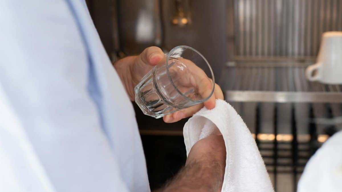 A person drying a glass with a towel in an indoor kitchen setting.