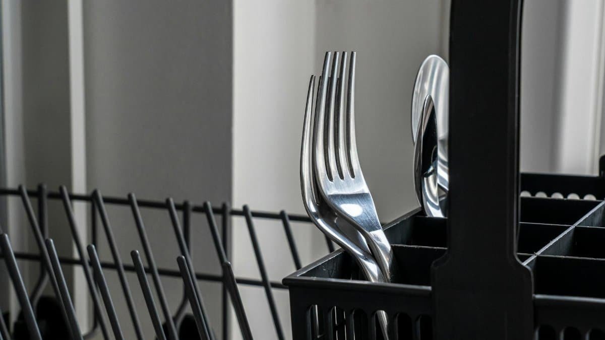 Close-up of stainless steel forks in a dishwasher rack, reflecting light and showcasing modern kitchenware.