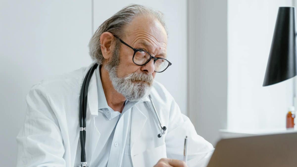 Elderly doctor using telemedicine for virtual consultation in office.