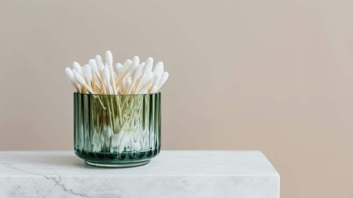 Aesthetic arrangement of cotton swabs in a green glass jar on a marble surface.