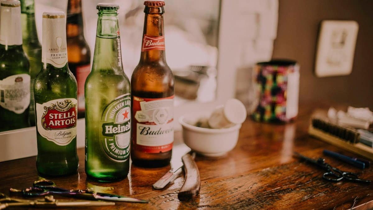 Beer bottles and barber tools on a wooden barbershop counter with a blurred mirror reflection.