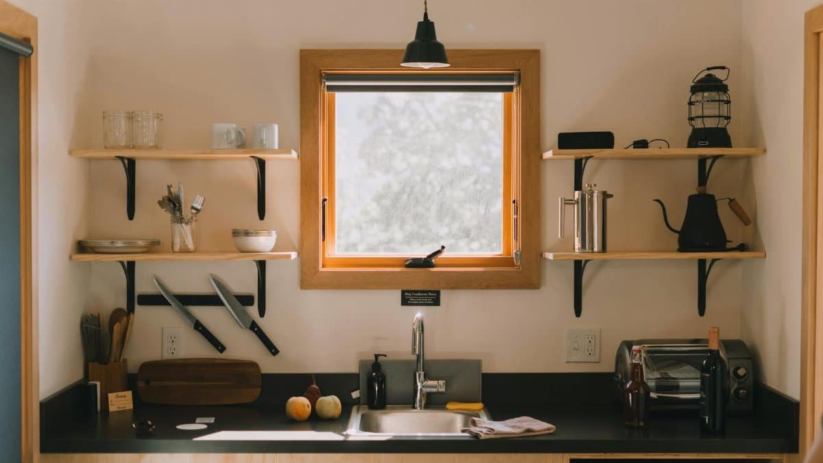 Modern kitchen interior with wooden shelves and hanging lamp above sink in light home