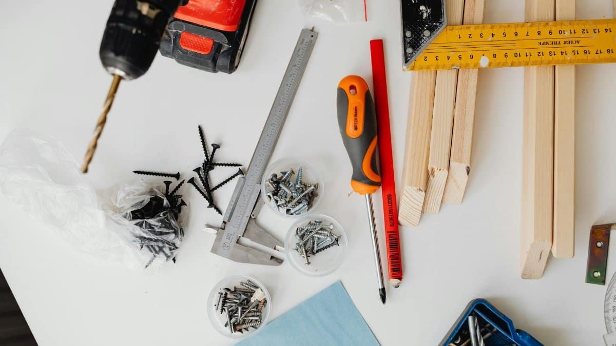 A collection of carpentry tools including drill, caliper, and try square on a white table.