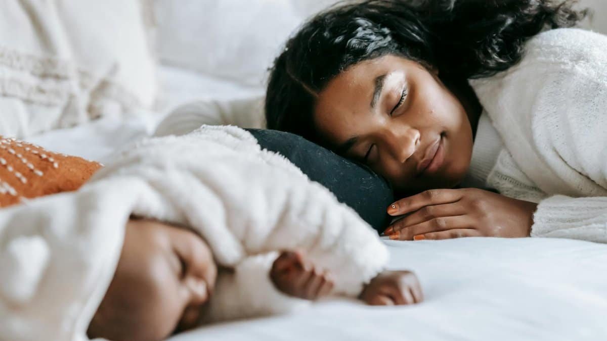 African American woman and infant baby lying on bed with white blanket while sleeping peacefully together during bed time at home