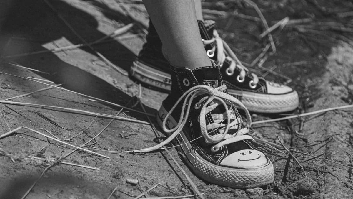 Close-up of worn Converse sneakers on ground, captured in black and white outdoors.