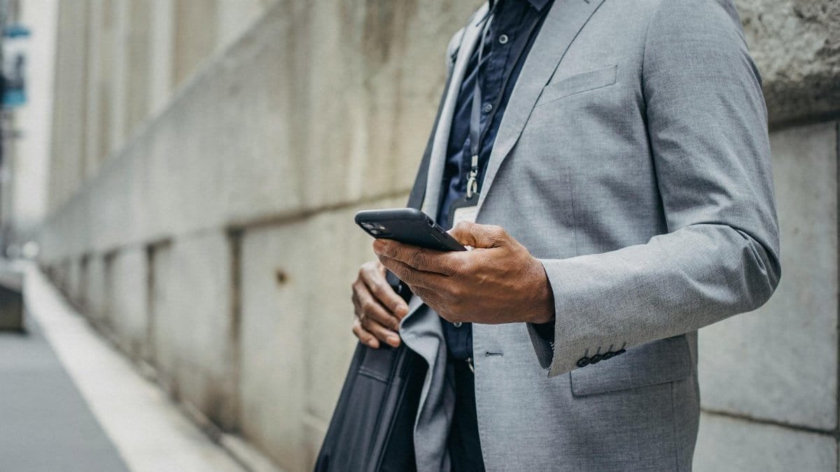 Crop unrecognizable African American male in formal suit standing on street and browsing modern mobile phone