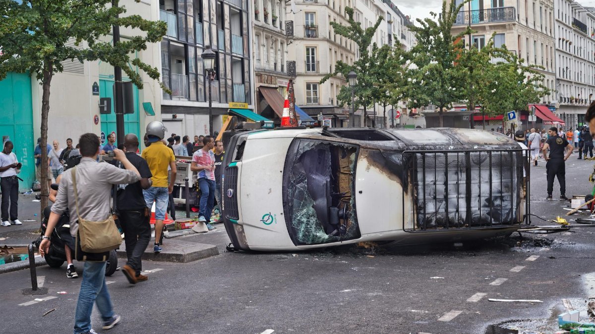 A busy city street with an overturned vehicle and gathered crowd capturing the moment.