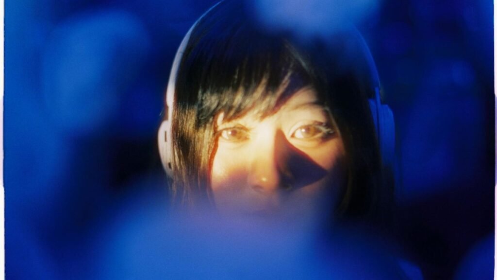 Artistic portrait of a woman with headphones, in a vivid blue, moody setting.