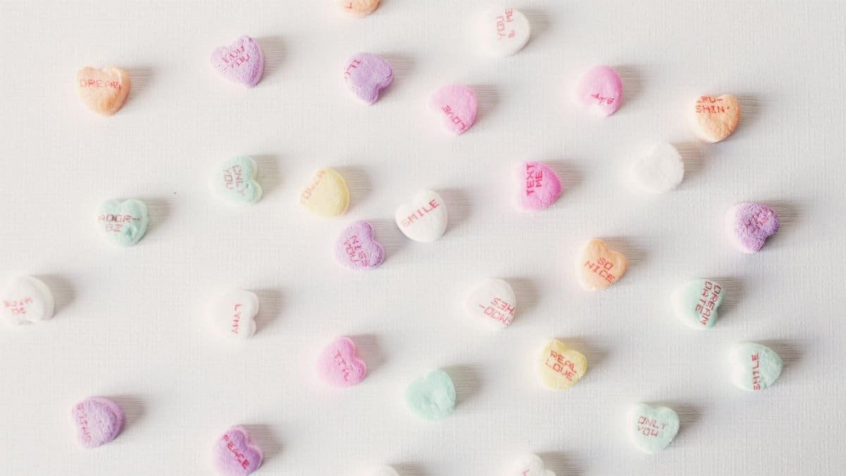 Top view composition of multicolored small heart shaped sweets placed on plain white surface