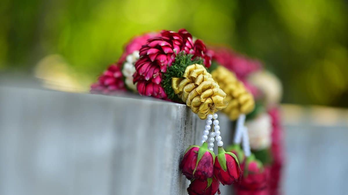 Colorful floral garland with roses and beads, resting on a concrete wall outdoors.