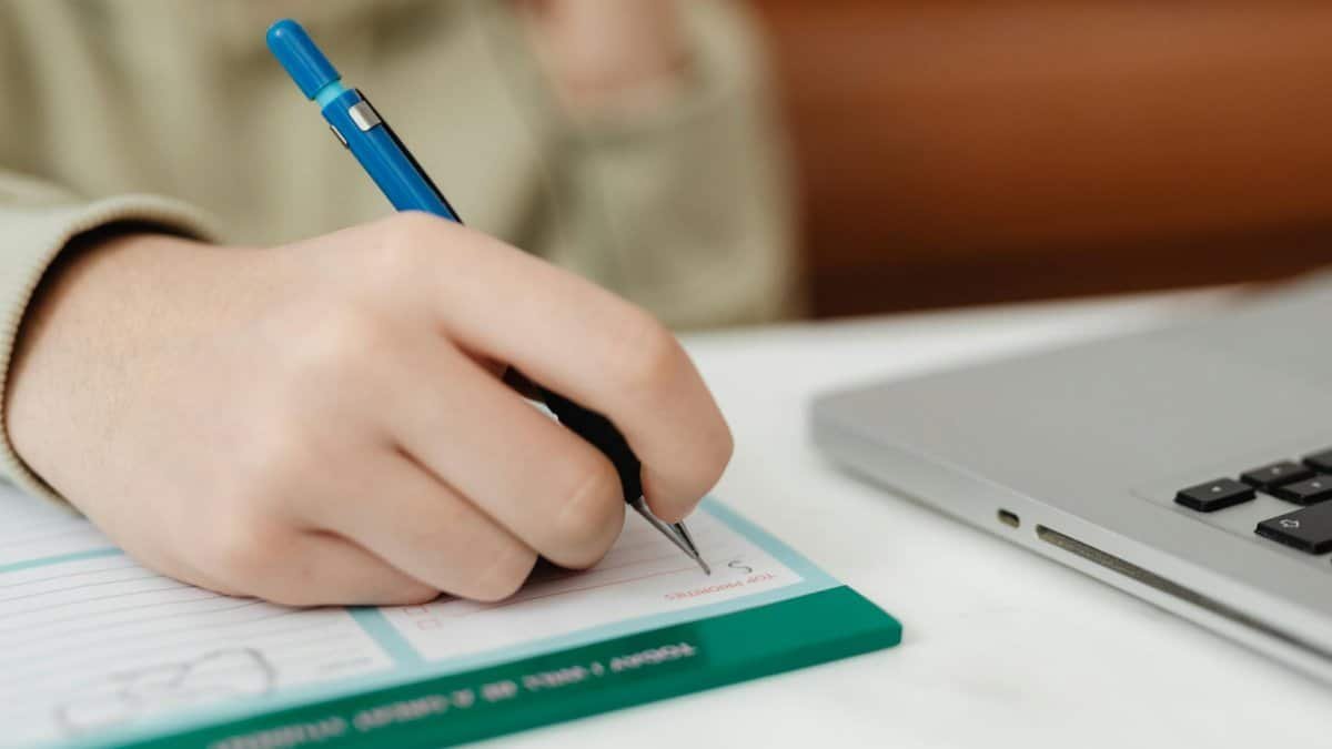 A close shot of a hand writing on a notepad near a laptop, suitable for productivity concepts.