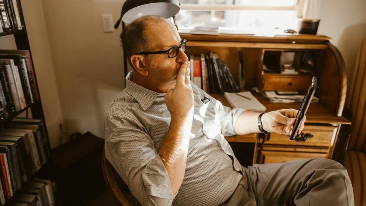 A middle-aged man wearing eyeglasses, engaged in a video call in his cozy home office.