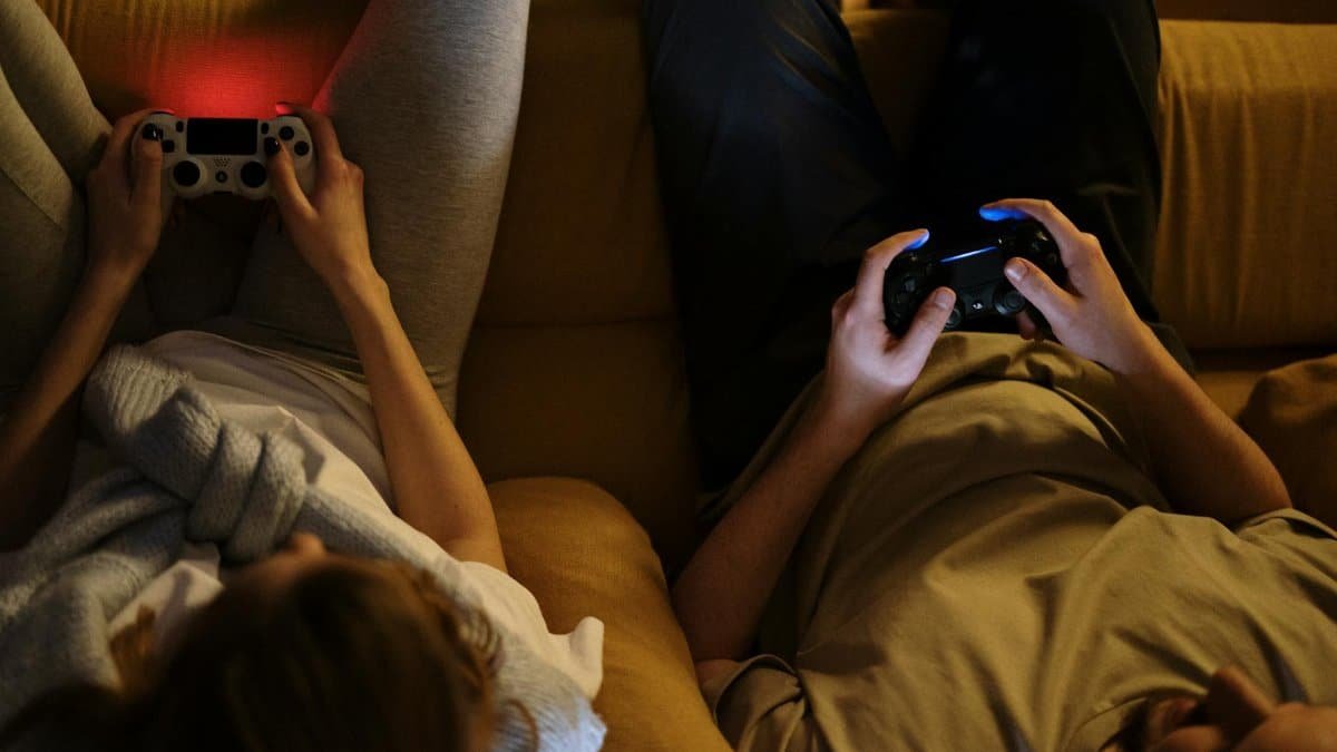 A couple enjoying an evening playing video games together on the sofa in cozy home lighting.