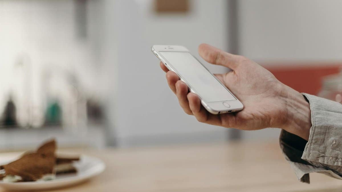 Person holding a smartphone in a cozy modern kitchen, showcasing technology in daily life.