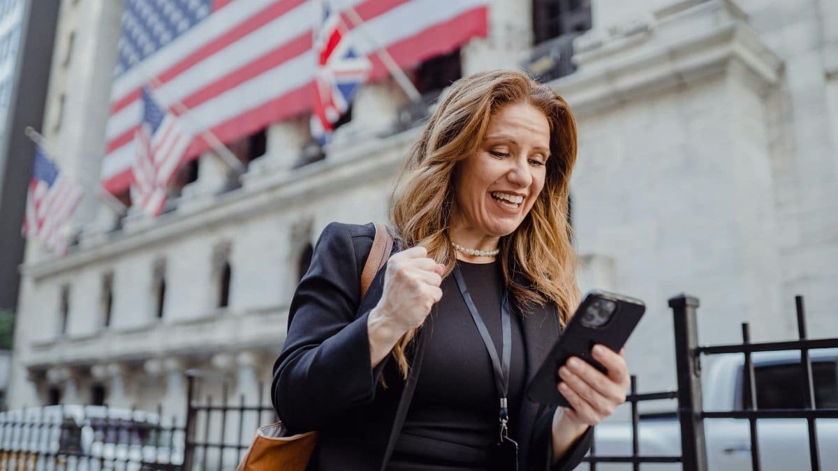 Smiling woman celebrates success while checking mobile phone near iconic city building with flags.