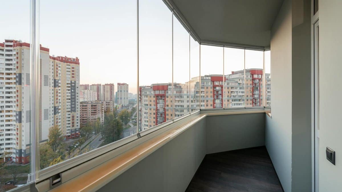 A modern balcony with glass panels overlooking a city's high-rise buildings at sunset.