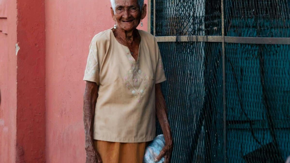 Smiling senior woman standing outdoors against a colorful wall.