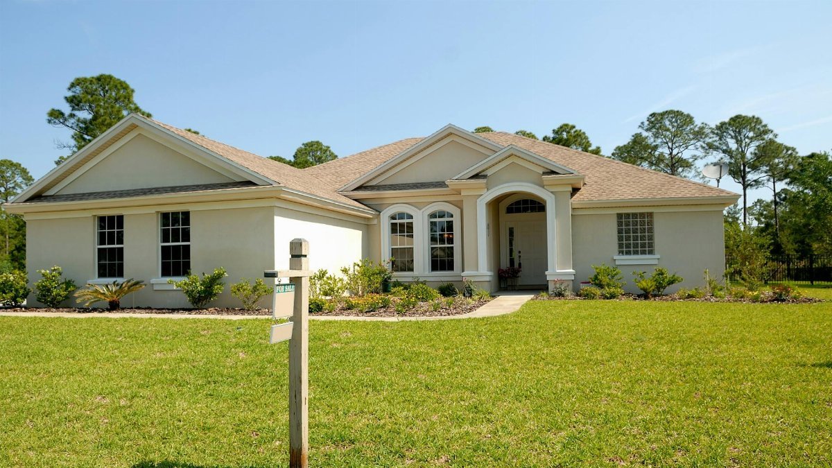 Beautiful suburban house with lush lawn, showcasing a for sale sign under a clear blue sky.