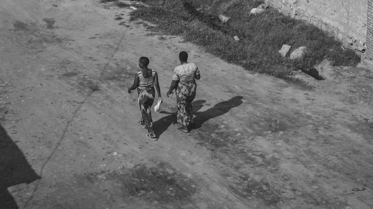 Black and white photo of two people walking down a dirt road in a rural area.