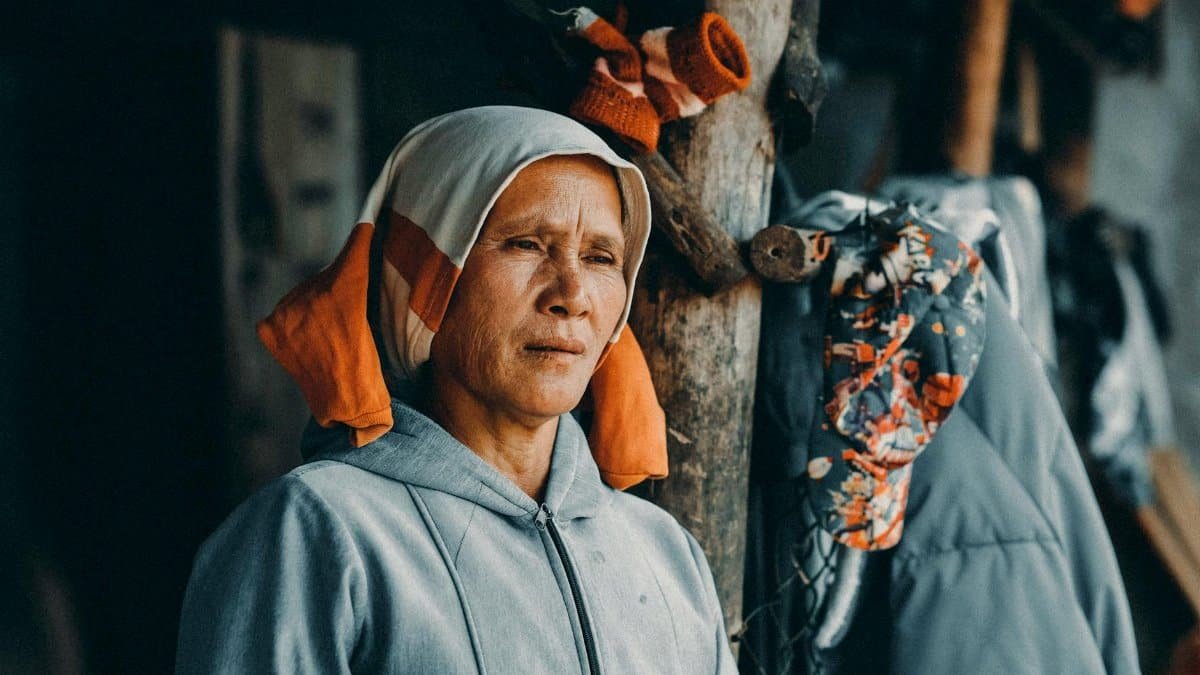 Elderly woman with headscarf in rural outdoor setting, capturing candid moment.
