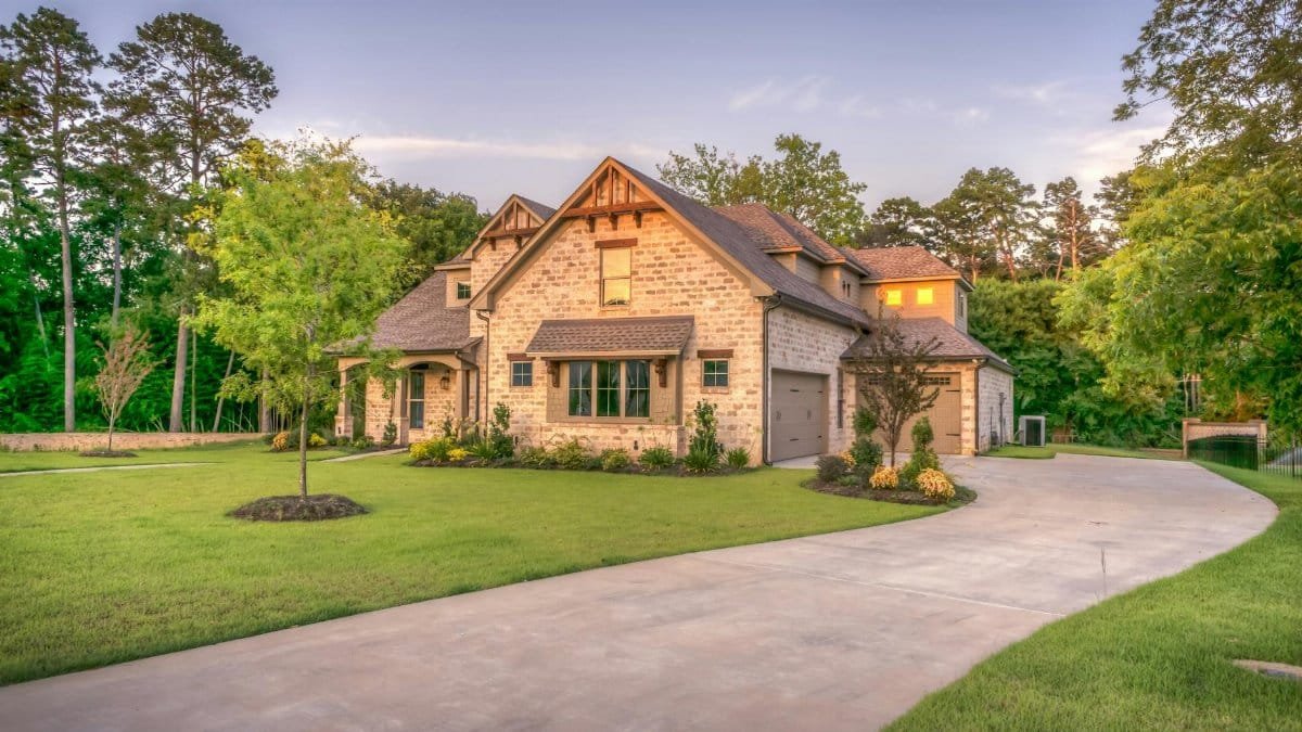 Elegant stone family home surrounded by trees, lush lawn, and vibrant garden.