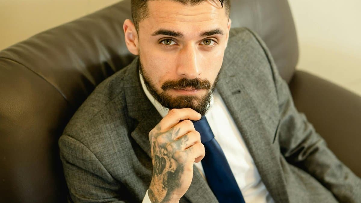 Portrait of a bearded businessman with formal attire sitting confidently indoors.