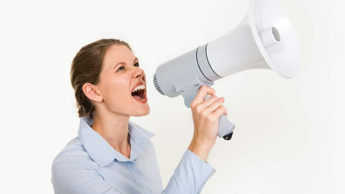 Energetic young woman shouting through a megaphone, expressing enthusiasm and leadership on a white background.