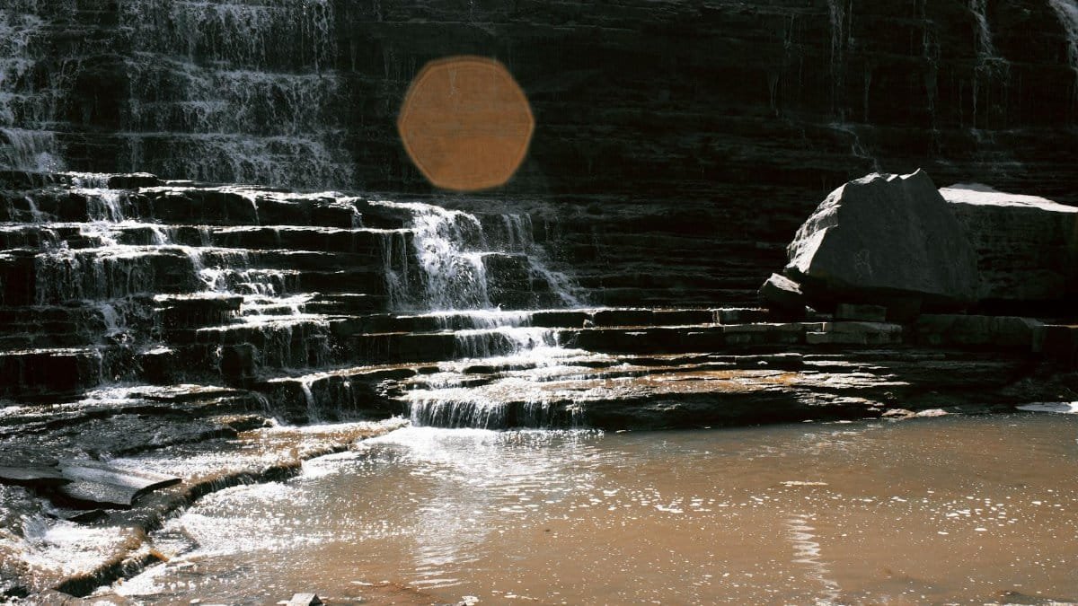 Natural waterfall with cascading water over rocky steps in a tranquil setting.