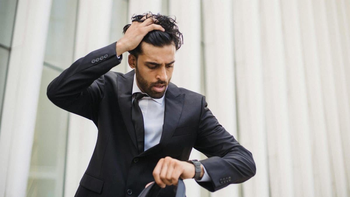A businessman in a suit checks his watch, expressing stress. Suitable for business themes.