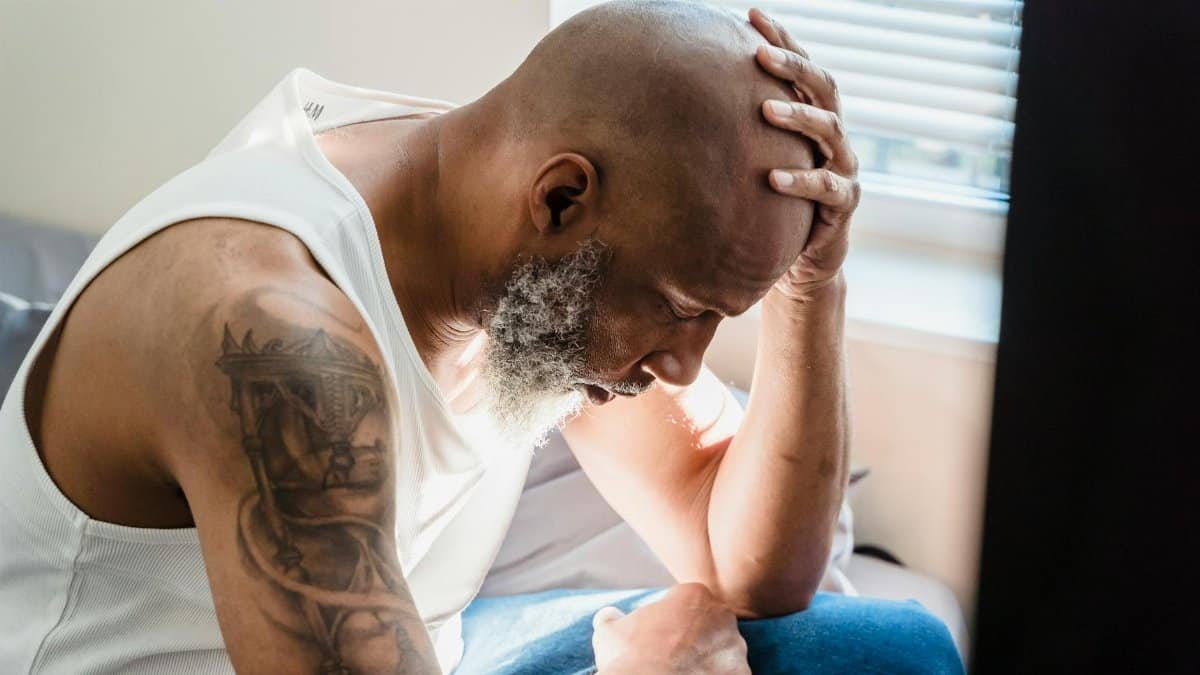 A senior man sits thoughtfully at home, conveying emotions of contemplation and stress.