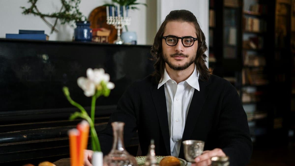 Jewish man with kippah enjoying Shabbat meal, surrounded by festive decorations.