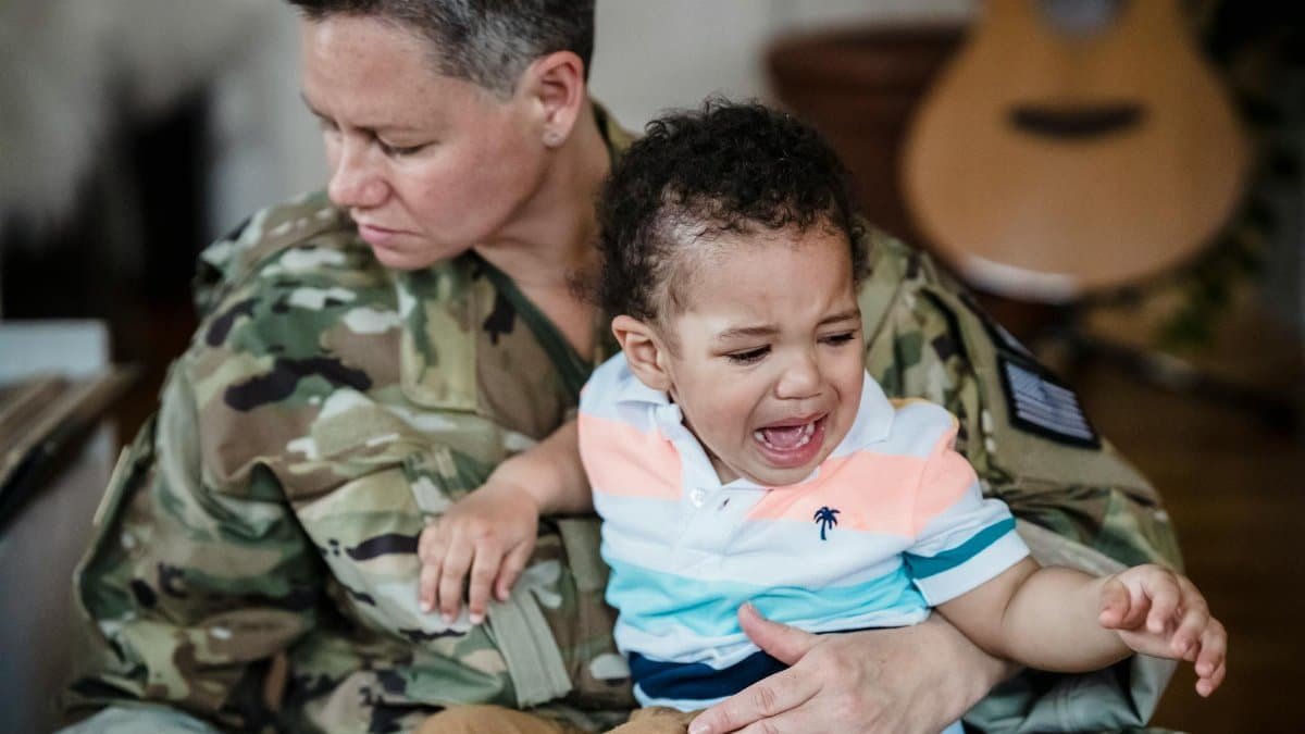 A soldier in uniform comforts a crying child, depicting the emotional bond and sacrifice of military families.