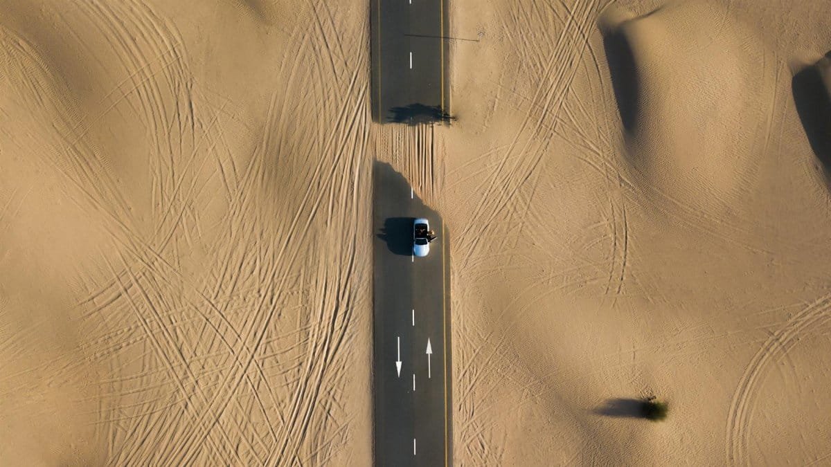 Aerial view of a road cutting through the sand dunes in Dubai's desert landscape.