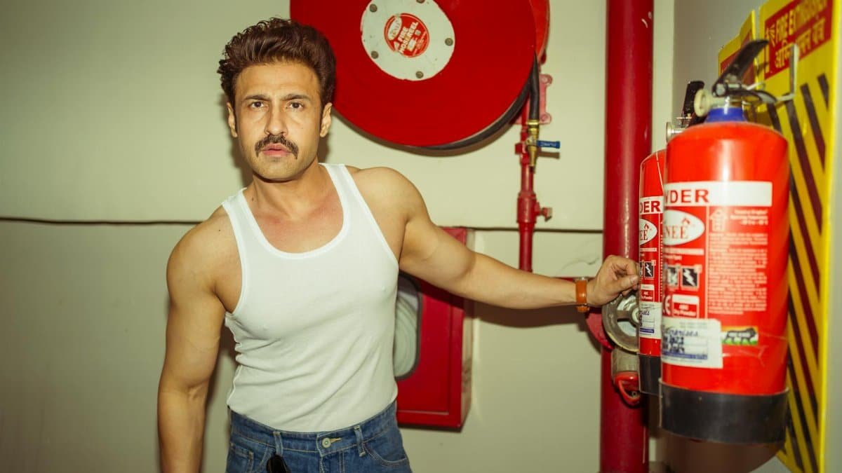A confident man in a tank top poses with a fire extinguisher in an indoor setting.