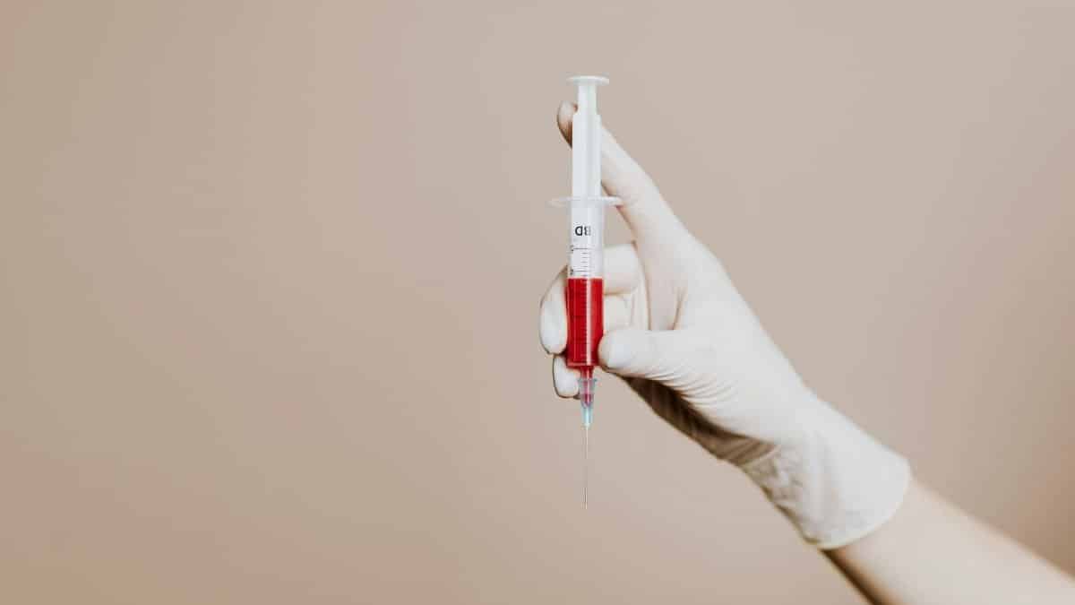 A gloved hand holding a syringe filled with red liquid, representing medical treatment or vaccination.