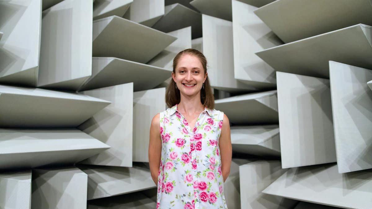 Smiling woman standing inside an acoustic engineering chamber with soundproof panels.