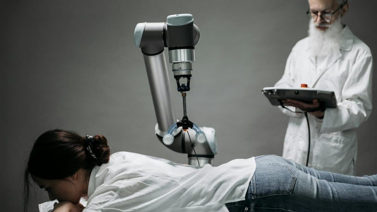 A woman receives a robotic massage as a scientist monitors, showcasing modern technology.