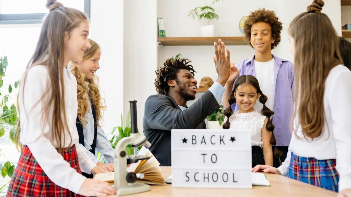 Happy students with a teacher celebrating 'Back to School' indoors.