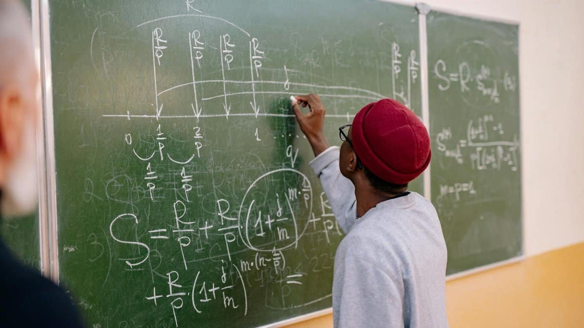 A young student writes mathematical equations on a green blackboard with precision and focus.