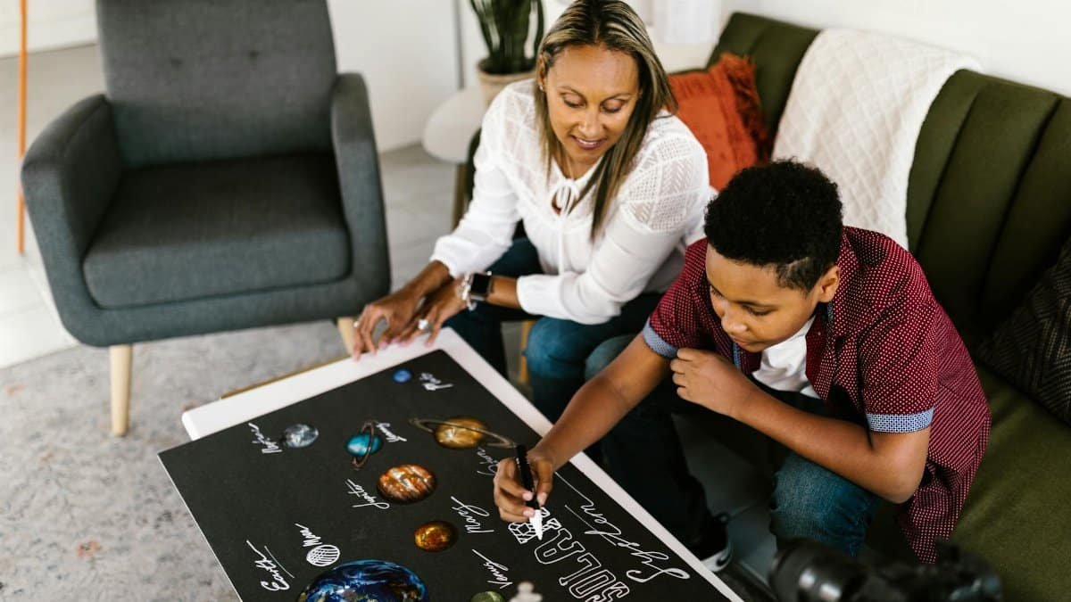 A mother and son collaboratively working on a solar system project indoors.