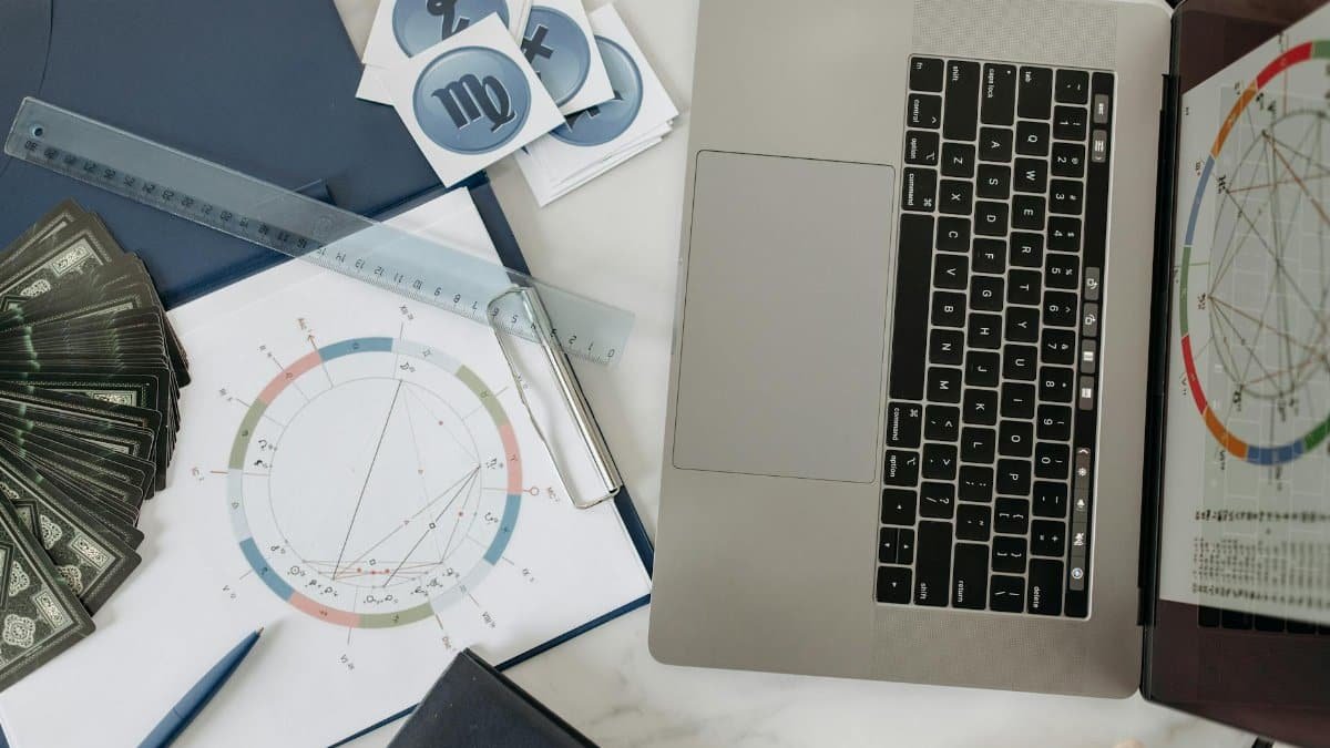 Astrology chart, laptop, and tarot cards on a desk, study of celestial influences.
