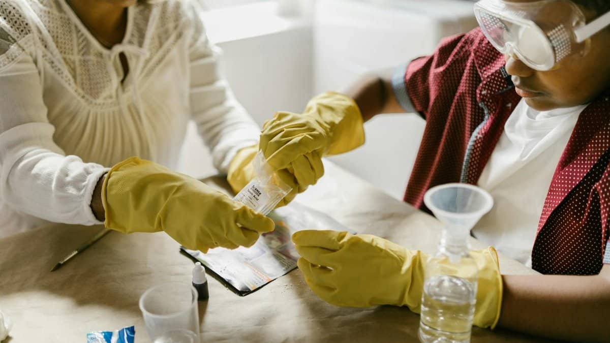 A mother and child conducting a science experiment with gloves and goggles indoors.