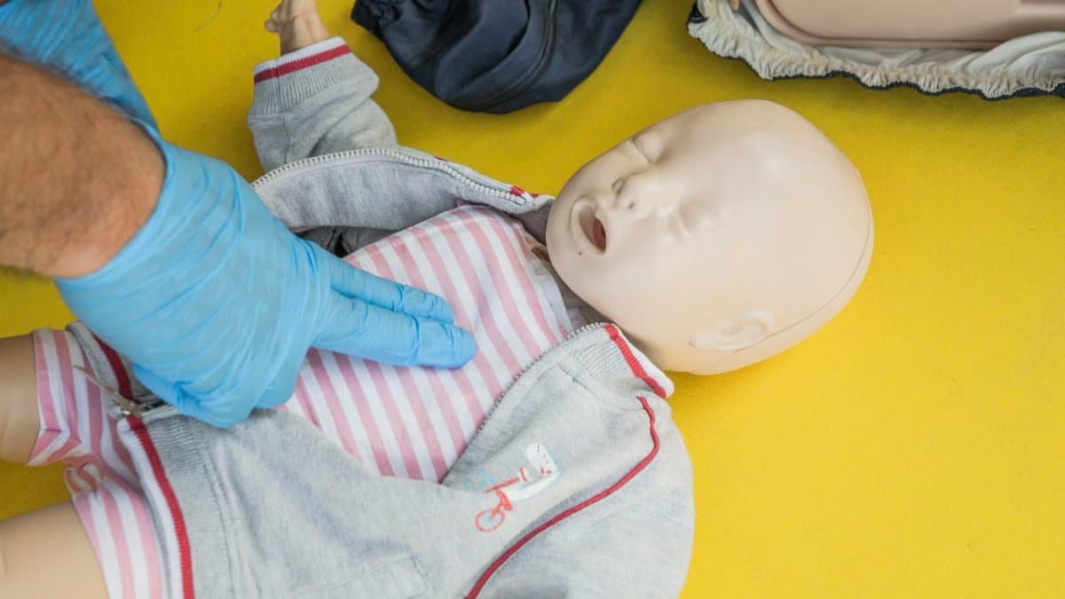A person demonstrates infant CPR on a manikin, highlighting first aid techniques.