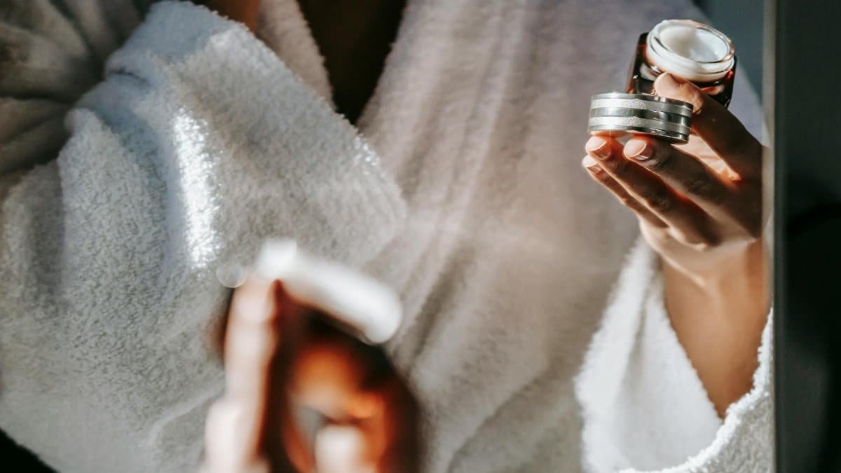 Woman in bathrobe applying skincare cream for a calm morning routine.