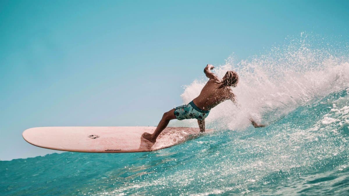 A male surfer skillfully maneuvers his board on a vibrant blue ocean wave under a sunny sky.