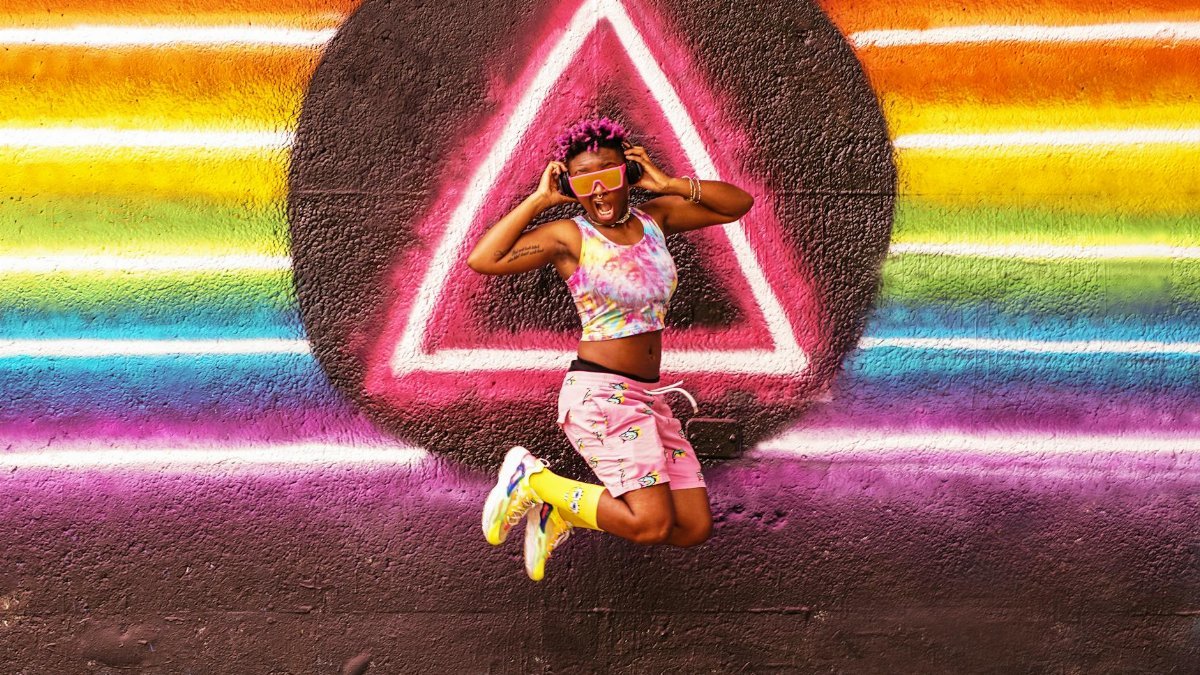 Vibrant image of a joyful woman jumping in front of a rainbow mural in Atlanta, Georgia.
