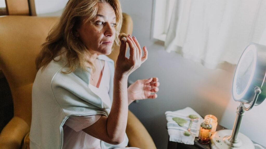 Woman indulging in self-care with a jade roller and candlelight ambiance indoors.