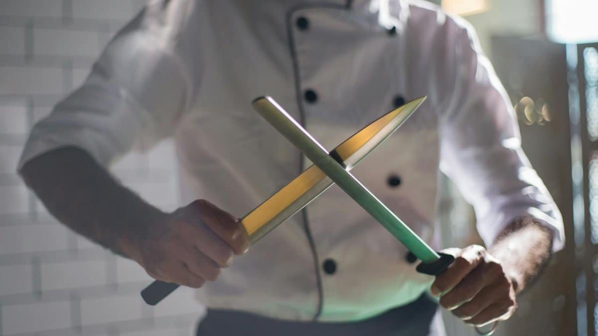 Close-up of a chef sharpening knives, emphasizing culinary skill and precision.