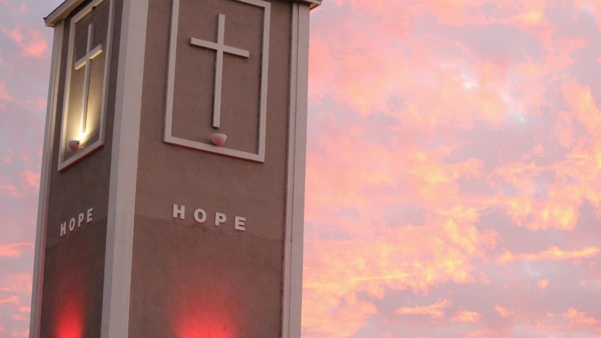 Illuminated church tower with crosses against a vibrant sunset sky.